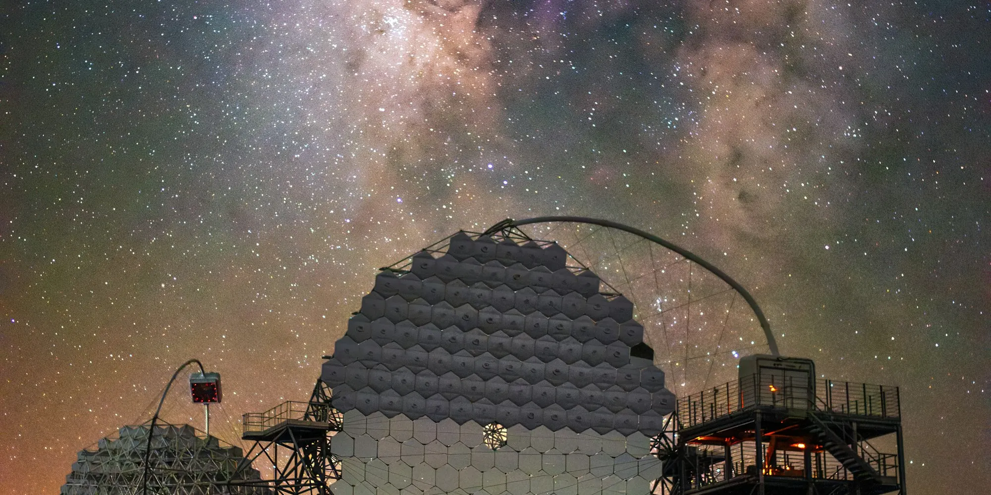 A large segmented-mirror telescope array under a dense Milky Way, at a mountaintop observatory