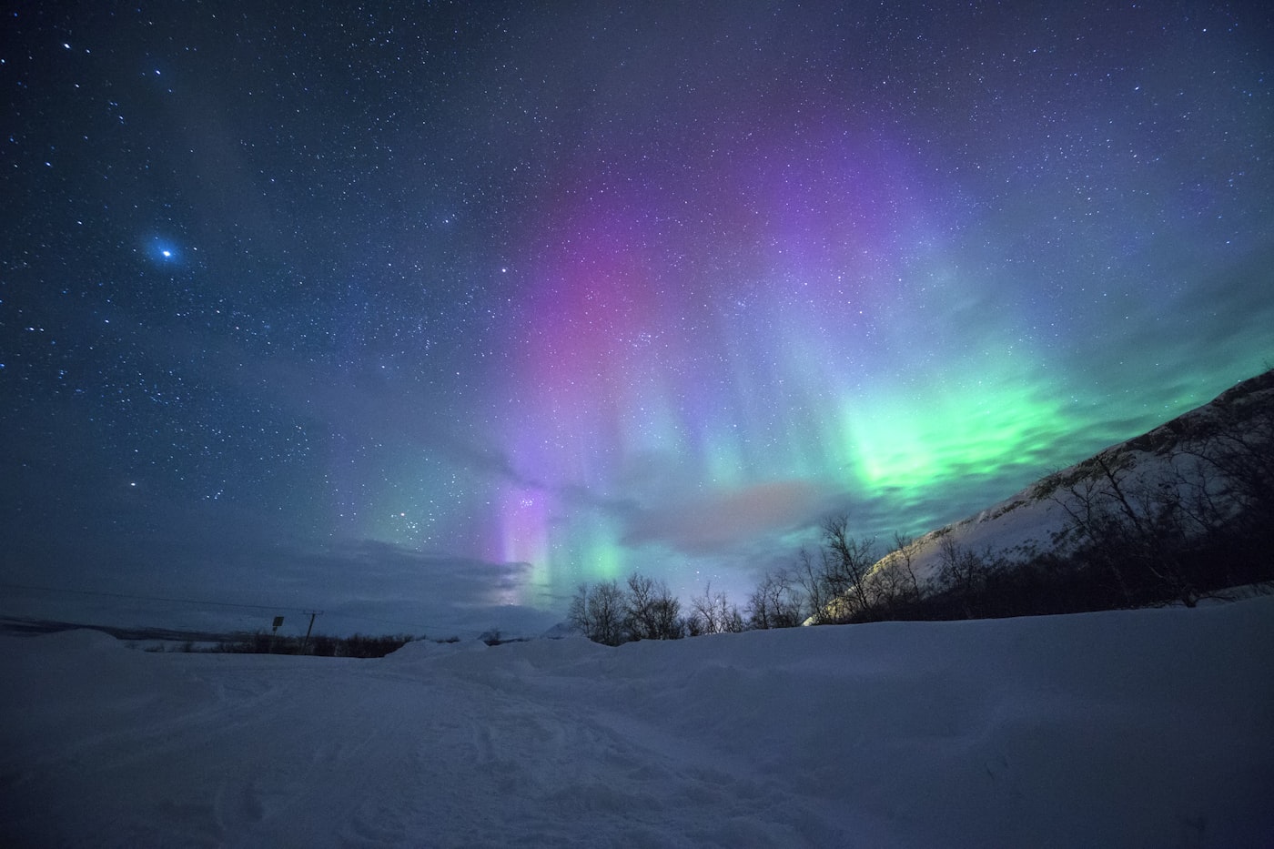 Green aurora borealis glowing over snow-capped mountains at night