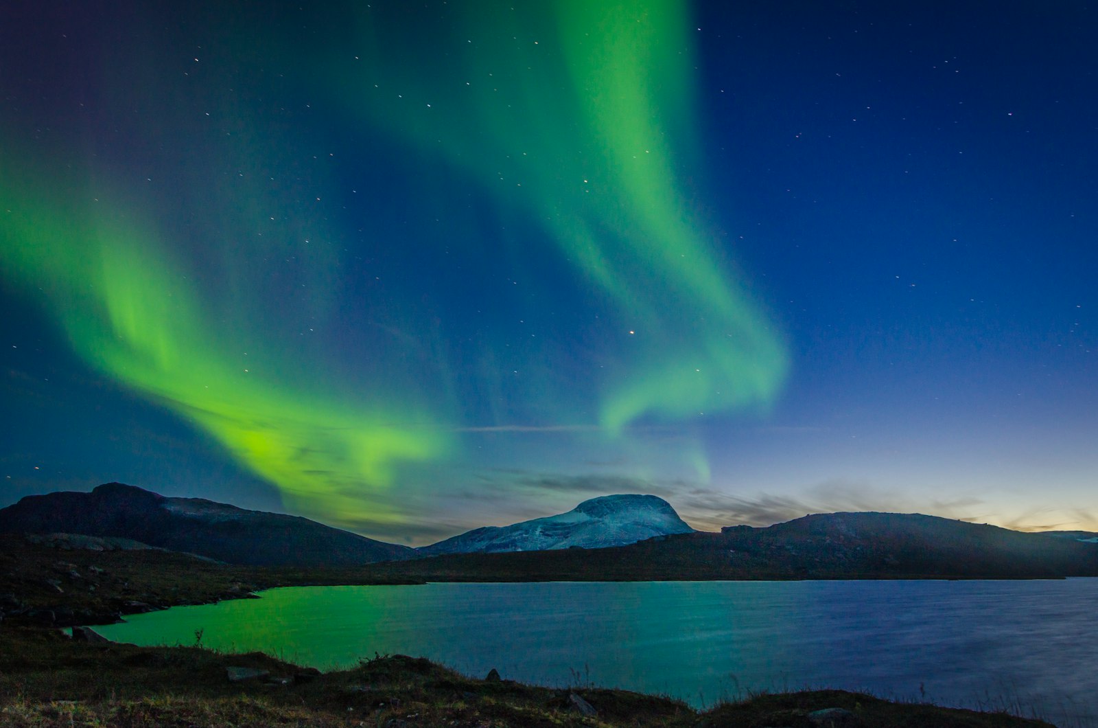 Aurora borealis glowing green and purple over a dark body of water at night