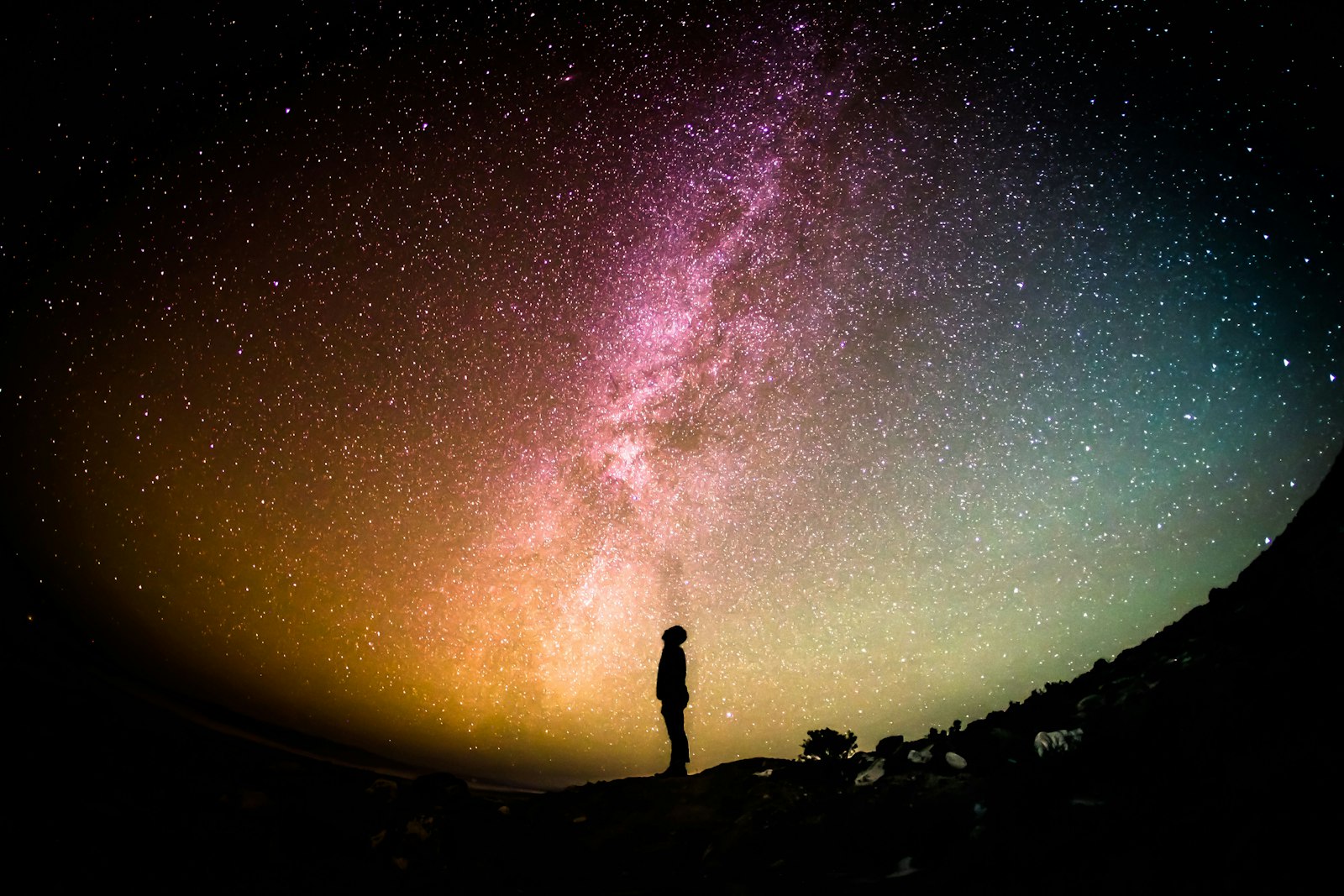 The Milky Way arcing over a still desert landscape at night, horizon glowing faintly