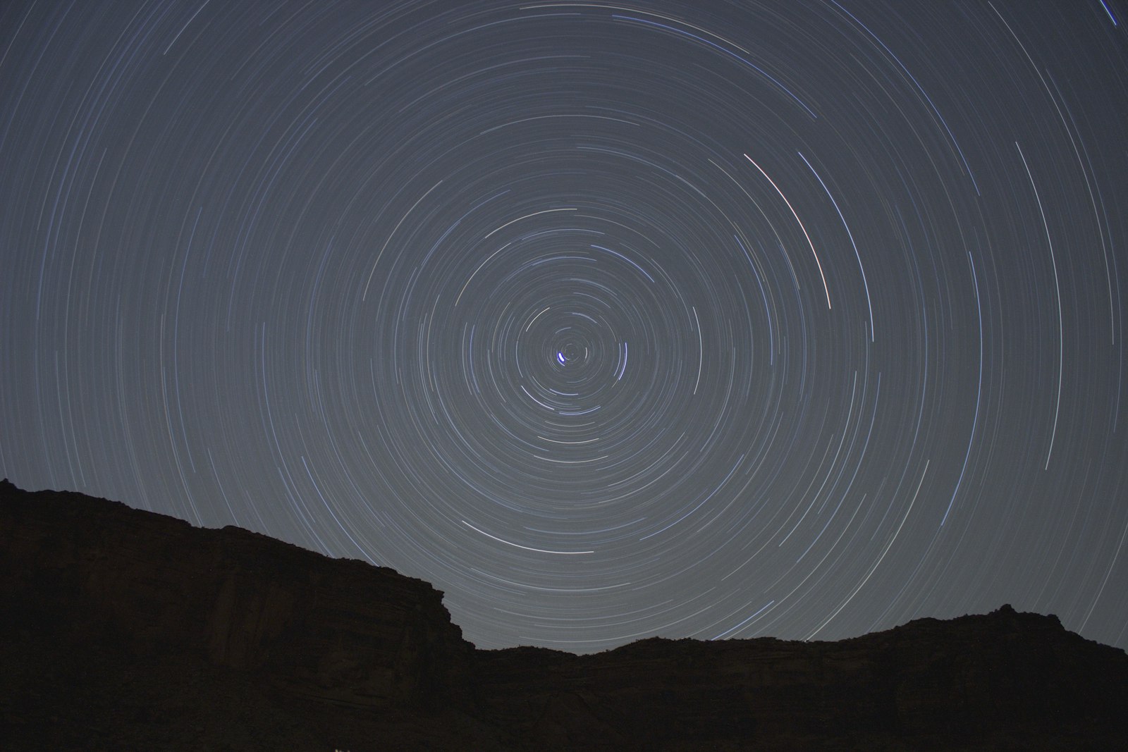Concentric star trails circling over a silhouetted rock face at night