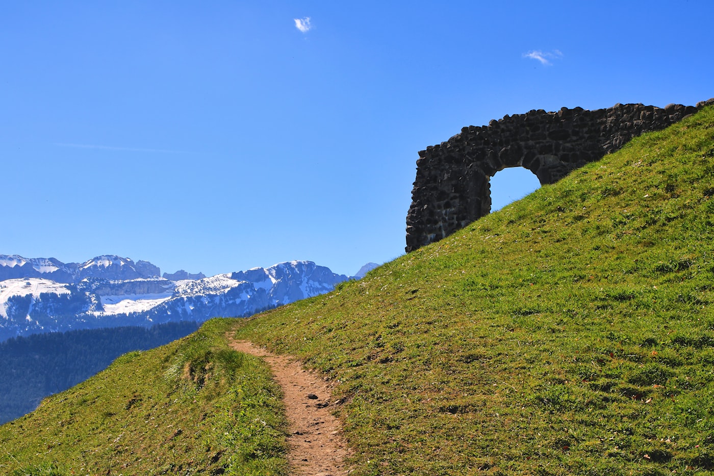 Stone archway ruins on a grassy hill beneath snow-capped mountains